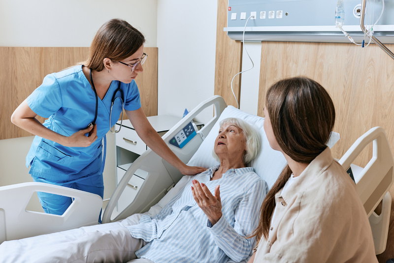 Elderly patient in hospital bed with caregiver and clinician